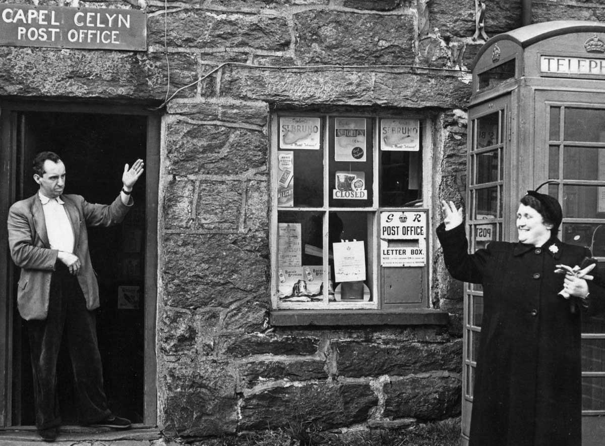 The postmaster outside his post office at Capel Celyn, Wales. Image: Wiki Commons.