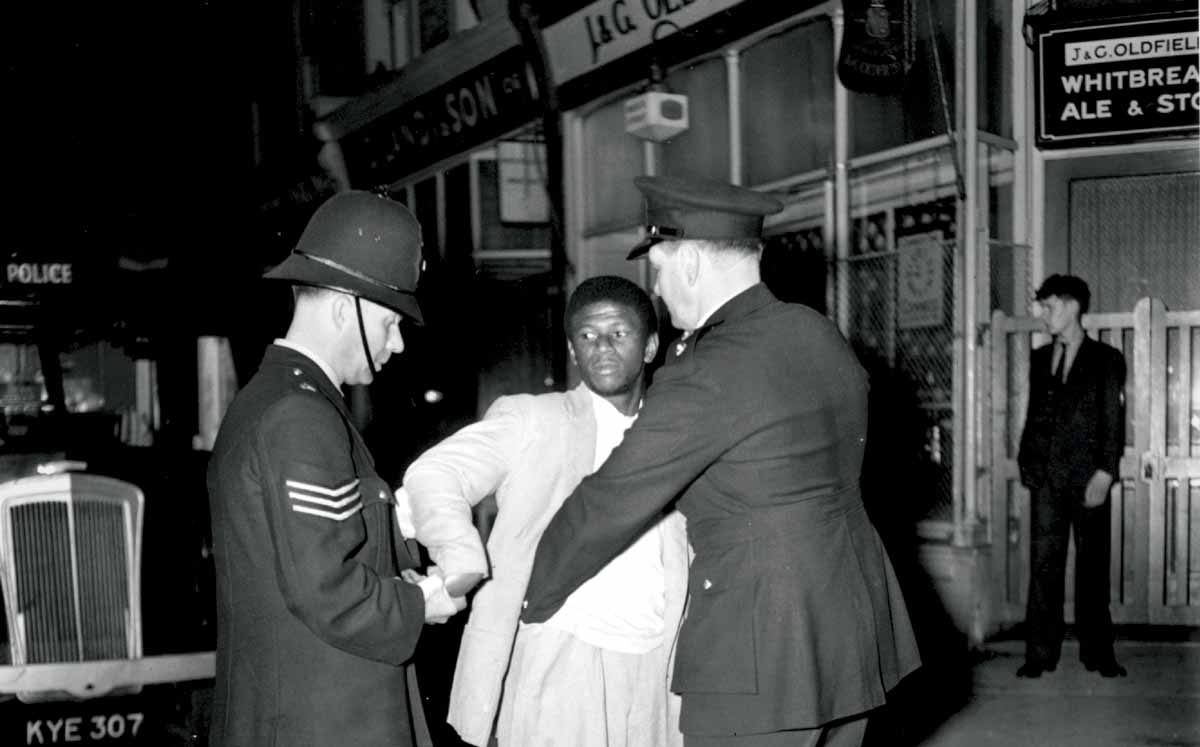London police search a black youth on Talbot Road, Notting Hill, during the race riots, 3 September 1958 © Getty Images.