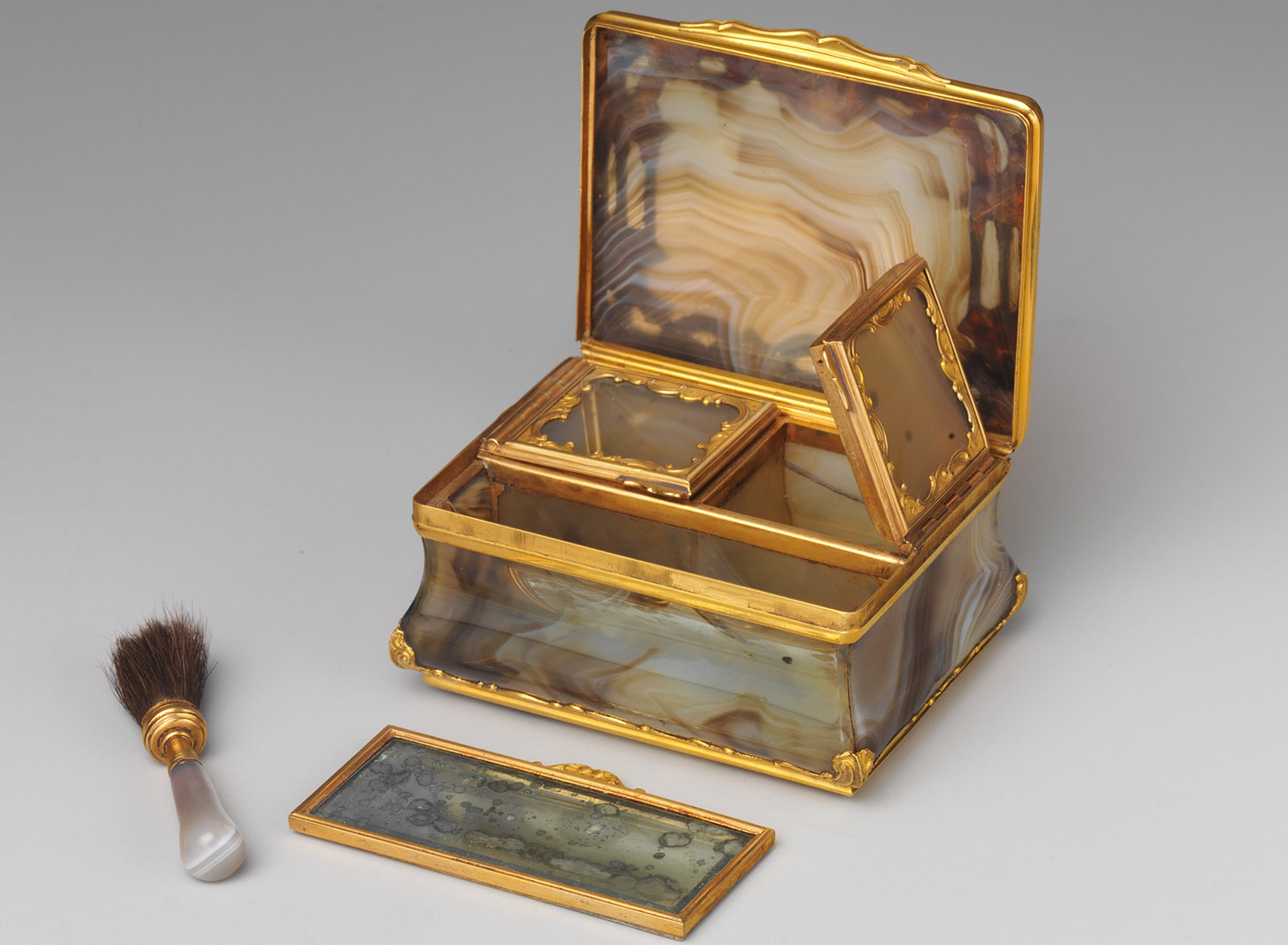 Resembling a snuffbox but smaller in size, this boîte à mouches contains two closed compartments—one to hold rouge and the other for black taffeta patches. A tiny brush and mirror were placed in the larger compartment.