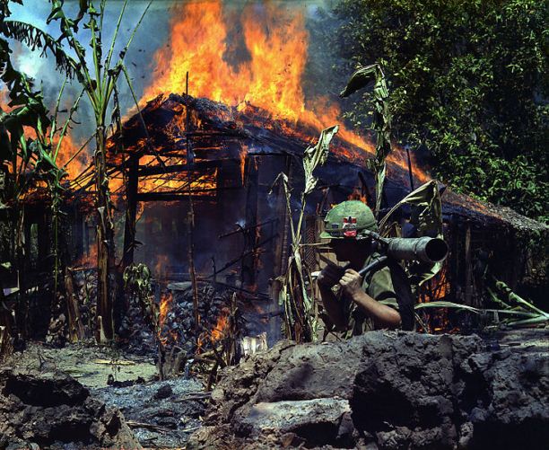 U.S. soldier carries a M67 recoilless rifle past a burning Viet Cong base camp in My Tho, South Vietnam, 1968