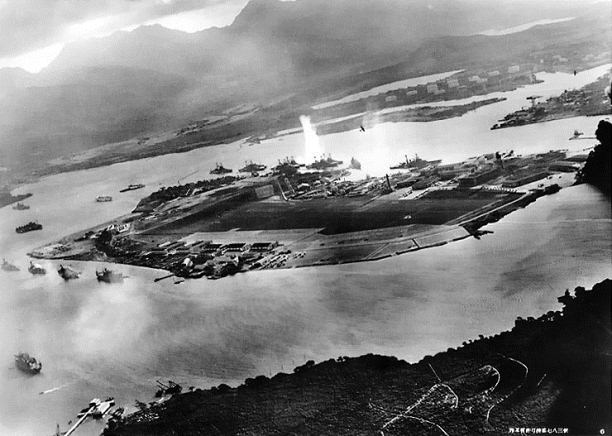 Photograph from a Japanese plane of Battleship Row at the beginning of the attack. The explosion in the center is a torpedo strike on the USS Oklahoma. Two attacking Japanese planes can be seen: one over the USS Neosho and one over the Naval Yard.