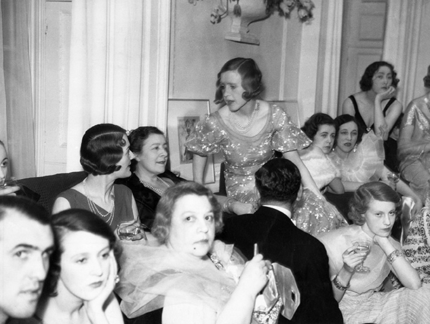 A fashionable crowd surround Syrie (wearing a dark dress and seated on the sofa) at a party given by the couturier Victor Stiebel at his Mayfair home, 1933. Getty Images/Hulton Archive