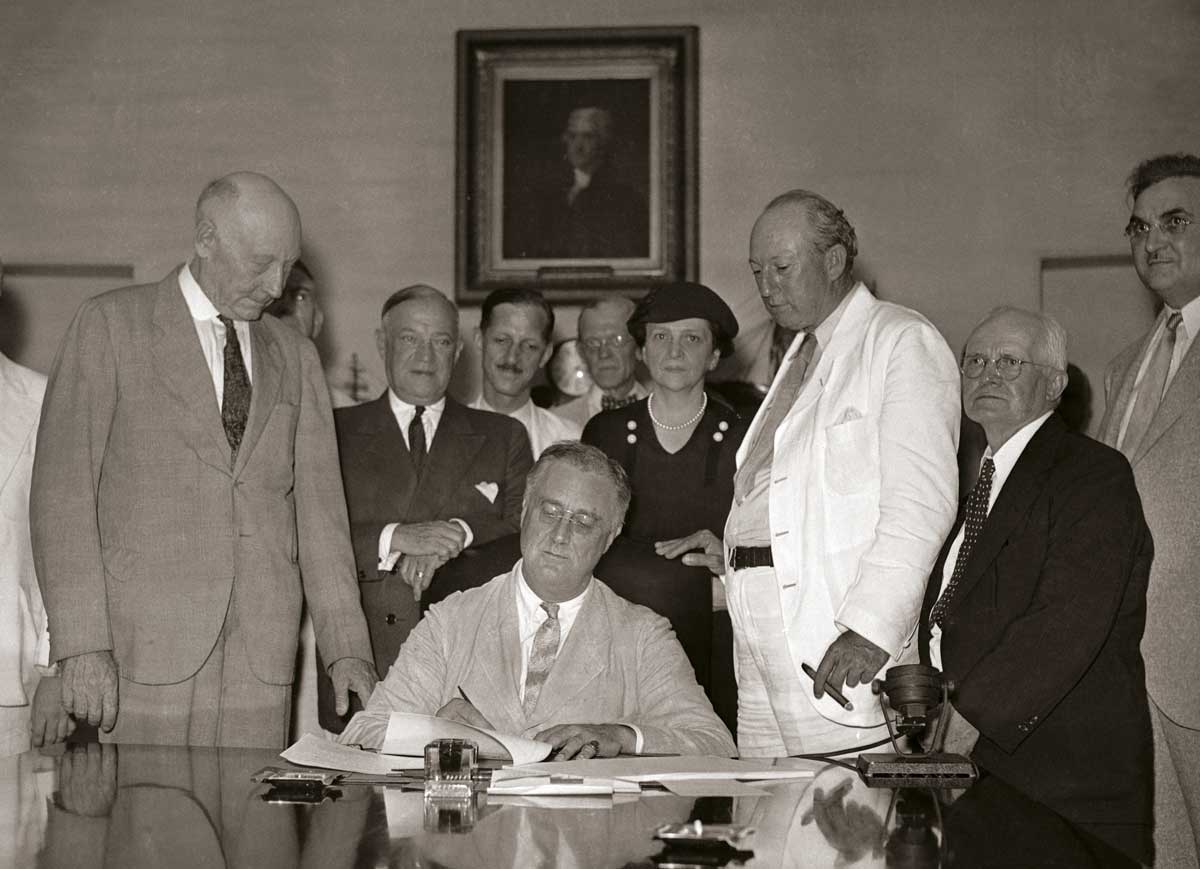 President Roosevelt signs the Social Security Act in the White House, 1935. Harrison is in the white suit © Getty Images.
