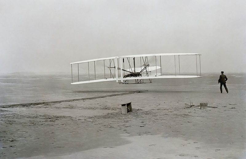 First flight of the Wright Flyer I, December 17, 1903, Orville piloting, Wilbur running at wingtip.