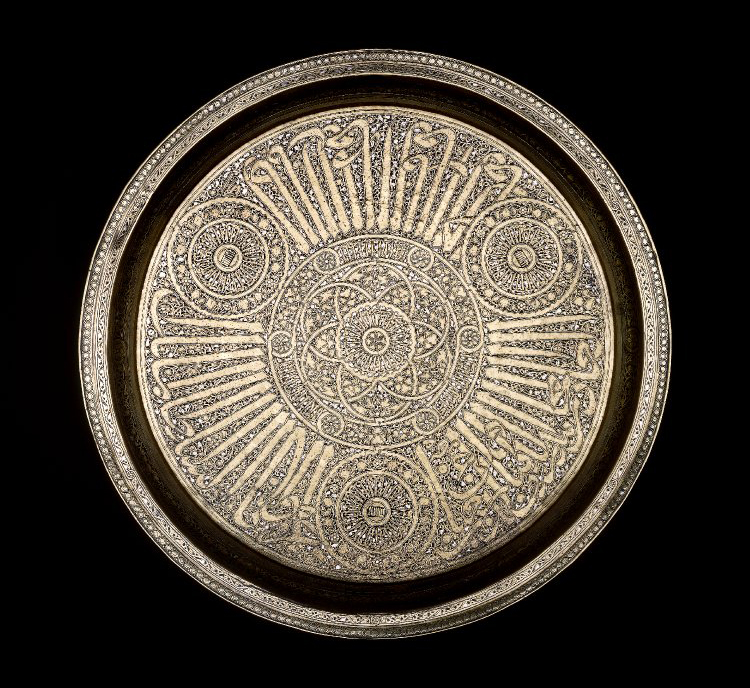 Sheet brass tray with curving cavetto and flaring rim. Decorated with titular inscriptions and the blazon of Sultan Sha’ban I (1345-46).