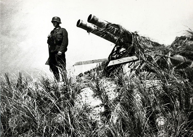 Quiet posting: a soldier in German uniform stands with a captured Dutch gun at Texel, May, 1940.