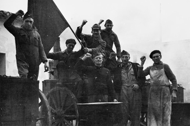 Members of the International Brigade in the British cookhouse at Albacete raise their fists in the Communist salute, December 1936 - January 1937, Elkan Vera. Courtesy of Imperial War Museums.