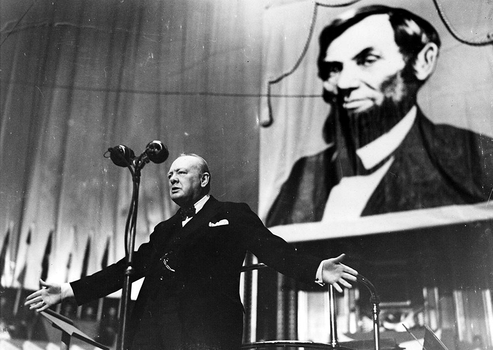Winston Churchill speaking at the Royal Albert Hall, London, in front of a picture of Abraham Lincoln, 1944.