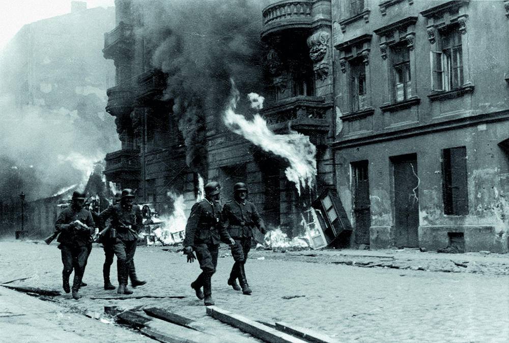 German soldiers walk through a burning street in the Warsaw Ghetto, 1943.