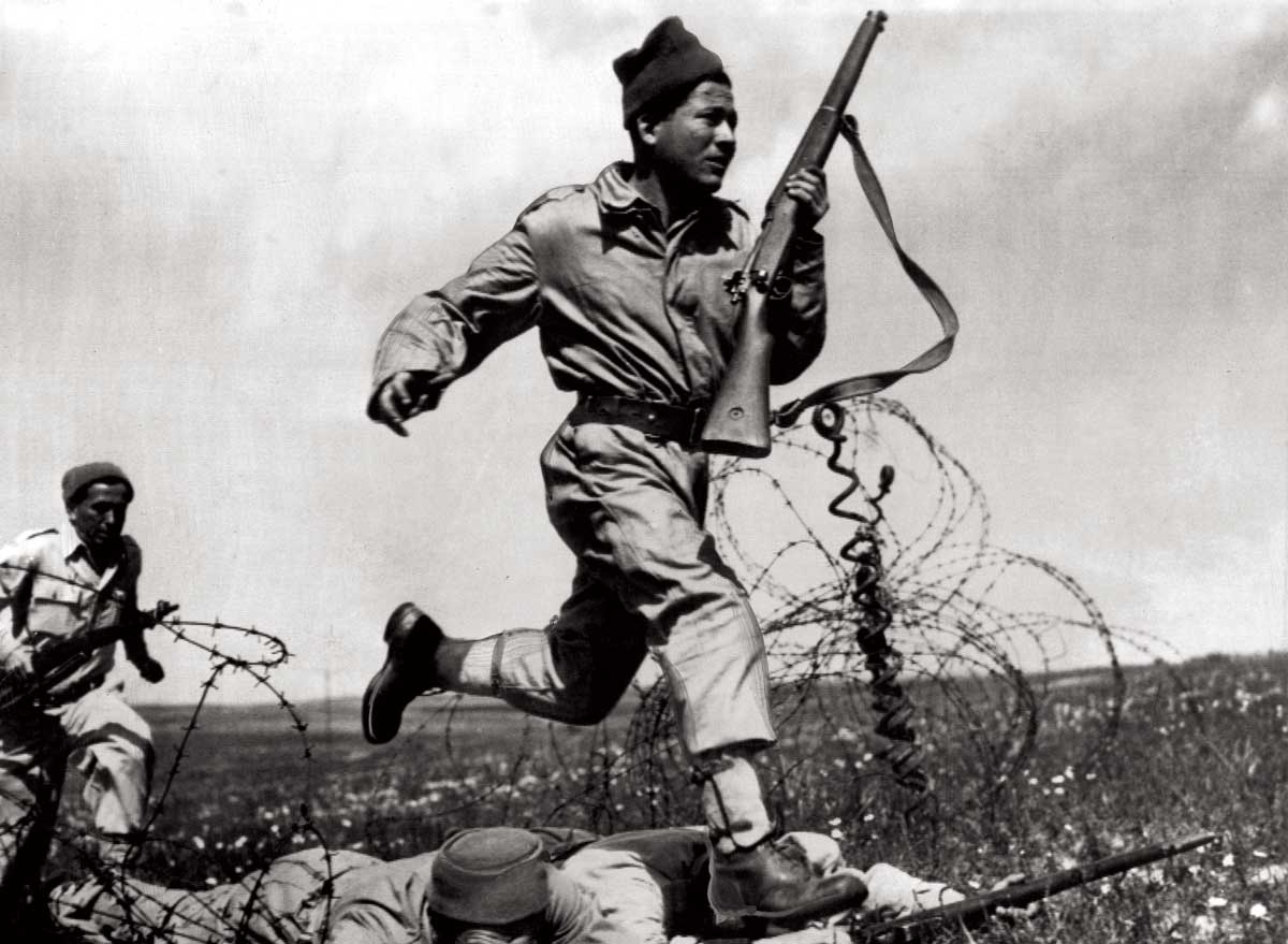 A Haganah fighter dashes across a human bridge formed by two comrades over barbed wire, Tel Aviv, 1948. 