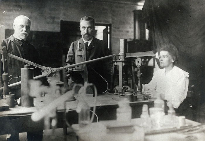 Marie and Pierre Curie (centre) in their laboratory, Paris, c.1900. Wellcome Collection. Public Domain.