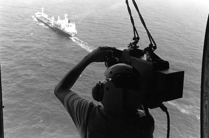 A cameraman films a tanker under US Navy escore in the Strait of Hormuz, 18 June 1988. National Archives and Records Administration. Public Domain.
