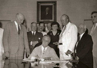 President Roosevelt signs the Social Security Act in the White House, 1935. Harrison is in the white suit. 