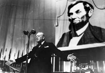 Winston Churchill speaking at the Royal Albert Hall, London, in front of a picture of Abraham Lincoln, 1944. Bridgeman Images.