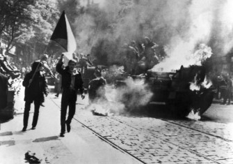 Czechoslovaks carry their national flag past a burning Soviet tank in Prague.