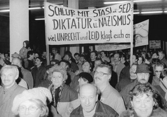 Citizens protesting and entering the Stasi building in Berlin; the sign accuses the Stasi and SED of being Nazi-like dictators.