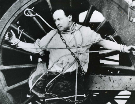 Harry Houdini strapped to a locomotive wheel, c.1910.