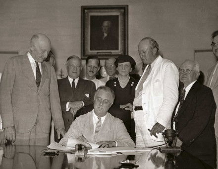 President Roosevelt signs the Social Security Act in the White House, 1935. Harrison is in the white suit. 