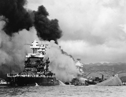 The U.S. Navy battleship USS Maryland (BB-46) alongside the capsized USS Oklahoma (BB-37) at Pearl Harbor. The USS West Virginia (BB-48) is burning in the background.