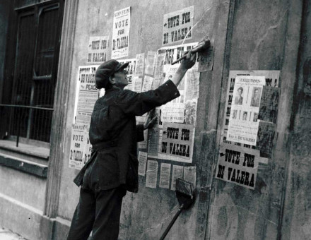 A man pastes over ‘Vote for de Valera’ election posters with arrest notices, Ireland, c.1923. 