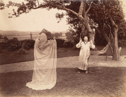 A Victorian double exposure photograph of a ghost in a white sheet frightening a man in a smock, c. 1887.