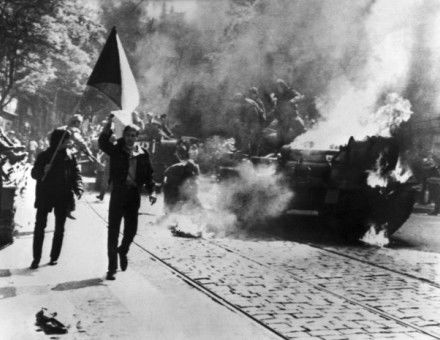 Czechoslovaks carry their national flag past a burning Soviet tank in Prague.