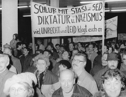 Citizens protesting and entering the Stasi building in Berlin; the sign accuses the Stasi and SED of being Nazi-like dictators.